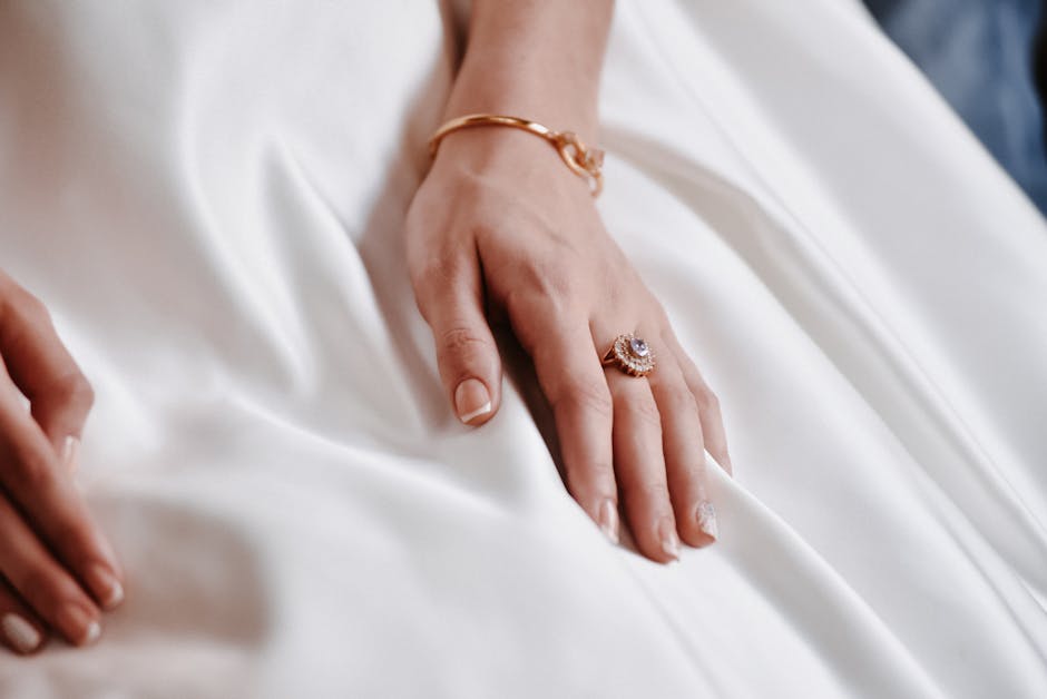 Close-up of a woman's hand adorned with a ring and bracelet on white satin fabric, showcasing elegance.
