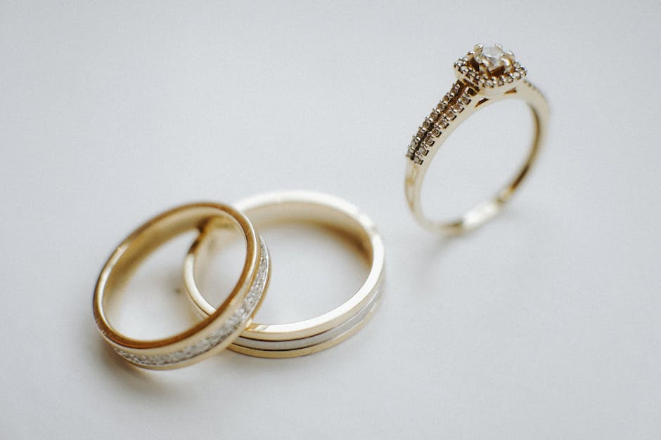 Elegant gold wedding bands and a diamond engagement ring on a plain background, ideal for wedding themes.